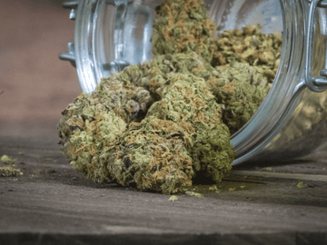 Glass jar with vibrant, trichome-covered cannabis buds on a rustic wooden surface.